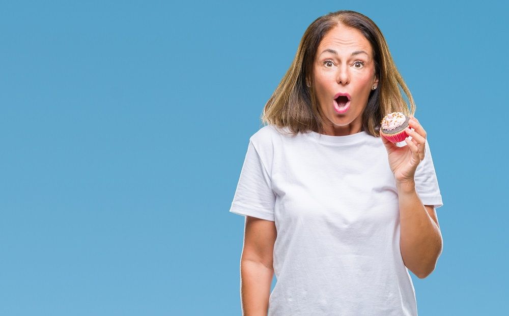 woman eating cupcake over isolated background scared in shock or surprise sugar and tooth decay preventative dentistry dentist in Medford New Jersey
